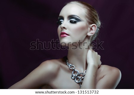 Portrait of a beautiful model in a dark evening fashion make-up on purple background wearing statement silver necklace