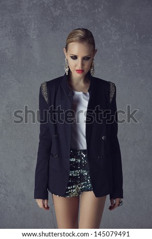 beautiful young blond woman with messy hair in a black blazer and sequin green shorts on grunge studio background