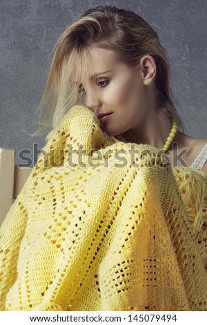 closeup of a beautiful woman with long blond hair sitting wrapped in crochet yellow blanket on grunge studio background