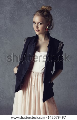 beautiful young blond woman with messy hair in a black blazer and pastel pink dress on grunge studio background