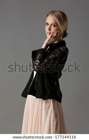 beautiful young blond woman with messy hair in a bun in a black lace jacket and pastel beige dress on studio background