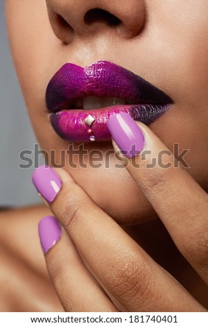 Close-up of woman's mouth with dark fashion purple lipstick with ombre effect. Hand with purple nailpolish touching tanned face