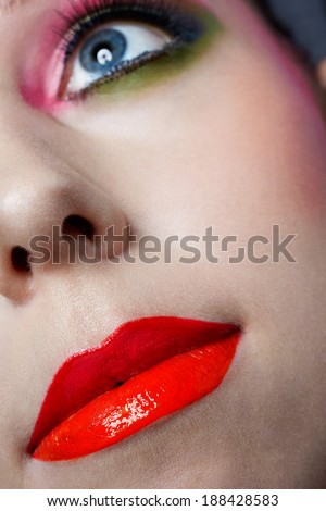 Closeup face of a woman with beautiful red orange lips and green eye makeup - studio shot of bright fashion makeup