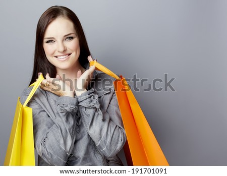 Portrait of a smiling young woman, with long brunette hair, on gray studio background, in luxury clothes, with bright shopping paper bags