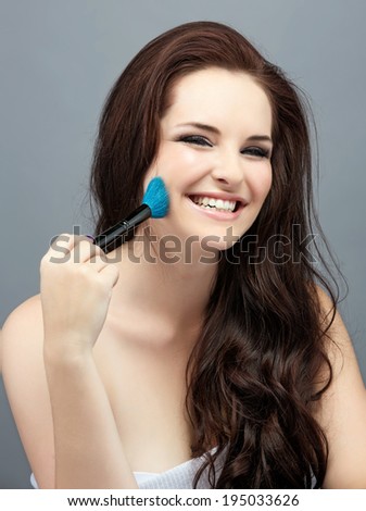 Portrait of the beautiful woman with bright makeup brushes near face, on grey studio background