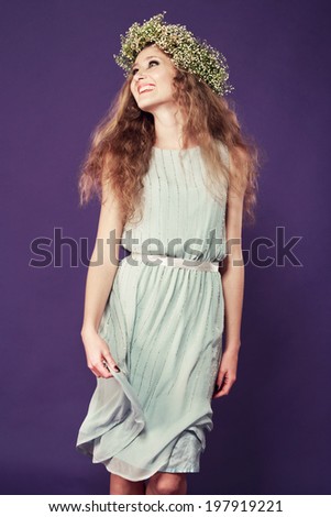 young woman with long blond curly hair and daisy flower wreath in a plain dress on studio background