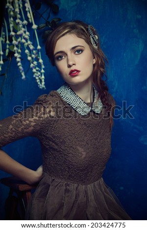 portrait of a beautiful woman with red hair in curly braided hairstyle. wearing a romantic lace dress and pearl collar on grunge wall background