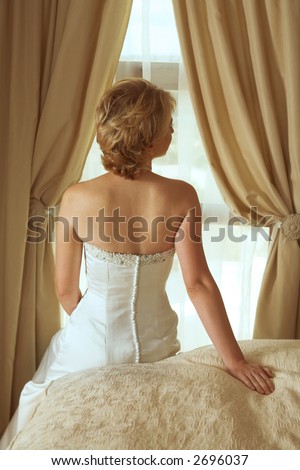 bride in beautiful pearl beaded white dress with short blond hair sitting on the bed in her bedroom
