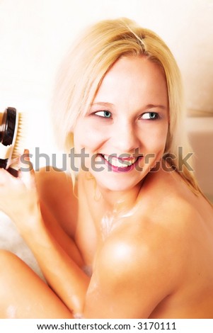 Young blond woman with a big smile sitting in bath with a body brush