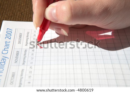 Woman marking a holiday date in a diary with red pen, focus on the red mark