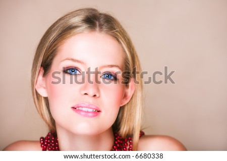 Blond teenage girl with loose straight hair on beige background with red shiny necklace and soft smile. Natural make-up,  has skin texture.