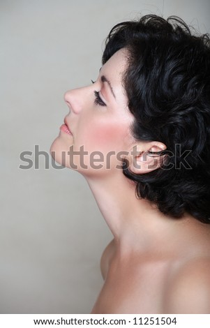 Beautiful woman in her early 40s late 30s with short curly black hair, in profile. Visible clear skin texture with pores and fine lines appropriate to her age, natural make-up