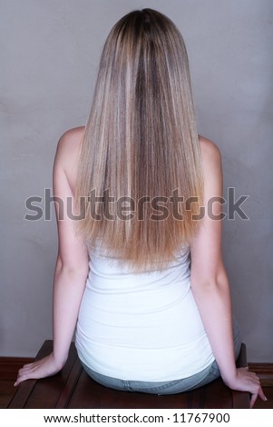 Young woman with long straight blond hair sitting in studio with her back - low key lit background