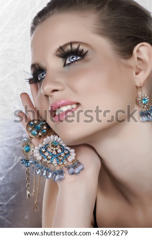 Blond woman with long fake lashes holding pearl and blue stones golden jewelry with happy expression from 16 Bit RAW