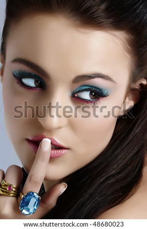 beautiful Italian model pressing finger on her lips in secret sign, with turquoise and pink make-up.
