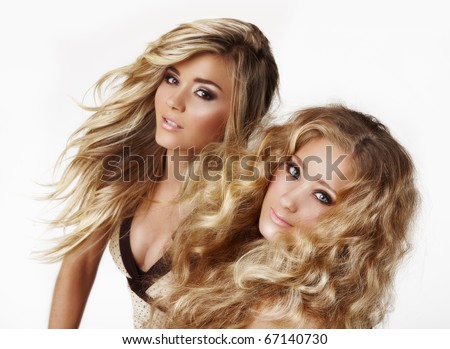 two beautiful blond woman sisters with styled blond hair blowing ion the wind on white background - not isolated.