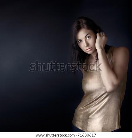 beautiful young woman with blue eyes and dark hair in structured bob haircut touching her hair with curious expression with copy space over dark blue background