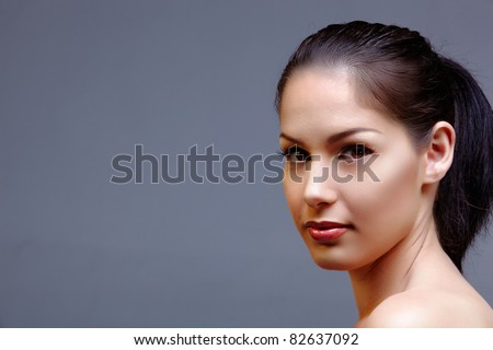 beautiful woman with long black hair in ponytail wearing classic natural make-up and beautiful skin texture over dark studio background with text space