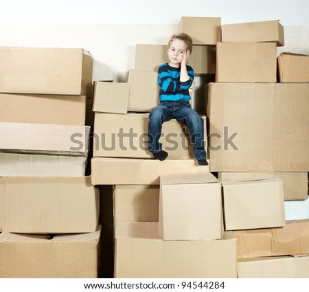 Reflective child sitting on the top of heap of carton packed boxes.