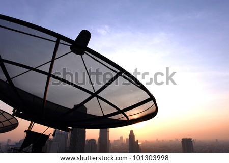 black antenna communication satellite dish over sunset sky in city