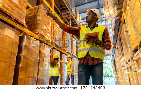 Portrait african black warehouse supervisor standing with digital tablet check stock in large warehouse distribution center with colleague worker in background. Business warehouse and logistic concept