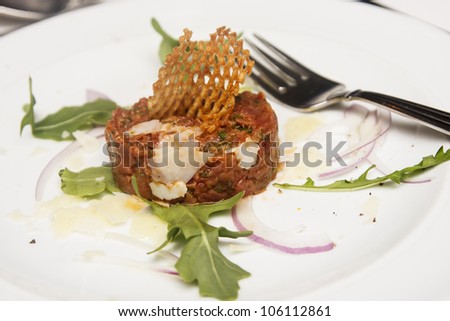Steak  tartar garnished with potato and arugula on white plate with a fork
