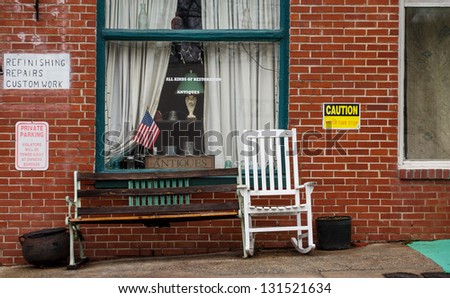 A small town antique shop with a bench and white rocking chair in front