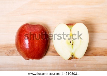 A red apple cut in half on a wood cutting board with skin side and cut side up