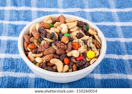 A bowl of trail mix with cashews, almonds, peanuts, raisins, and candy covered chocolates