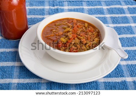 Hot, spicy chili in a white bowl with a spoon and bottle of hot sauce