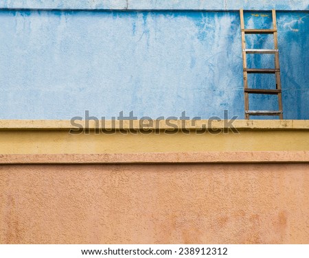 An old wooden ladder leaning against a blue stucco wall over yellow and orange walls