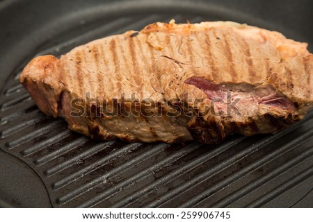 A strip steak grilling in a black iron pan