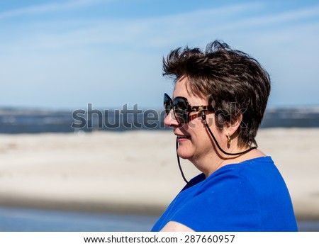 A nice looking older woman smiling on a beach looking into frame