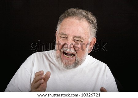 An older man in white tshirt on black background with an expression of pain or anguish