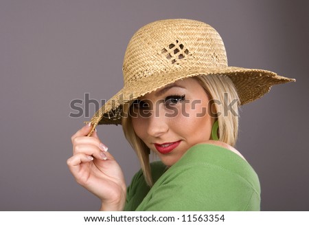 A blonde in green blouse and straw hat pulling the brim over her eyes