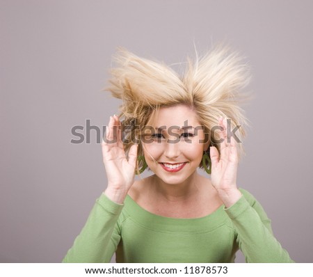 A blonde in green blouse with her hair flying and her hands held beside her head