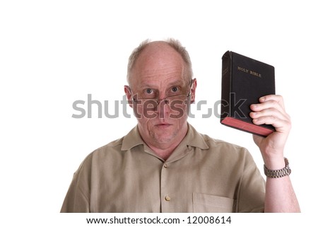 An older guy wearing a brown shirt and glasses holding a bible and looking at camera