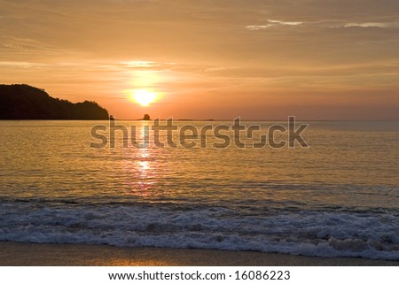 An orange sunset over rocks reflected in the surf below