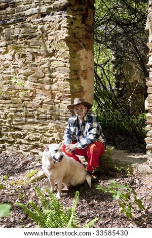 Hispanic Man in plaid shirt and orange pants with a dog by an old rock wall