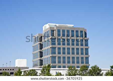 A square grey office building rising out of the trees against a clear blue sky