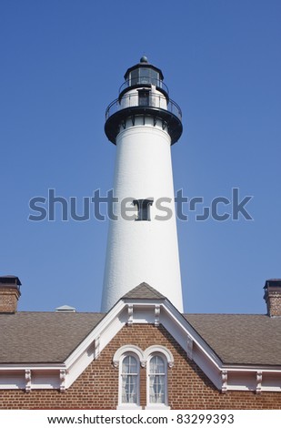 A white brick lighthouse beyond the roof of a red brick home