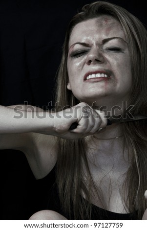 Beaten white woman holding a knife to her throat with a black background