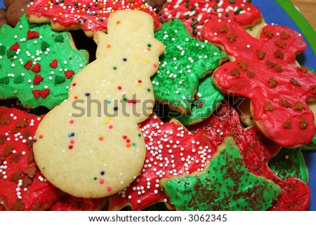 Snowman-shaped Christmas cookie on a pile of red and green cookies with sprinkles.