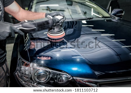 Man with orbital polisher in repair shop polishing car. Car detailing