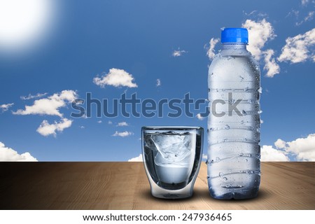 Cold Water Bottle and Glass Of Ice Cubes on Wood Table With Blue Sky Background