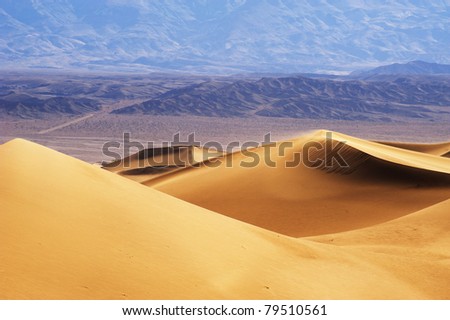 Strong wind blows the sand of the sand dunes in the desert with mountain in the background
