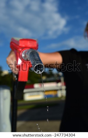 woman holding a dripping red gas petrol hose nozzle
