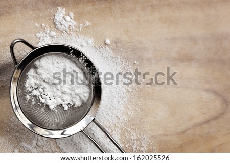Icing or confectioner\'s sugar in sifter, over baking paper.