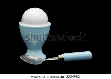 Living, breathing, and eating golf.  Golf ball in egg cup, with egg spoon, on black background.