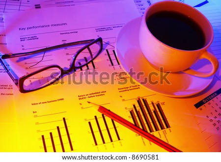 Late night checking financial performance.  Coffee for a caffeine boost, glasses and pencil on financial papers.  Warm tones.